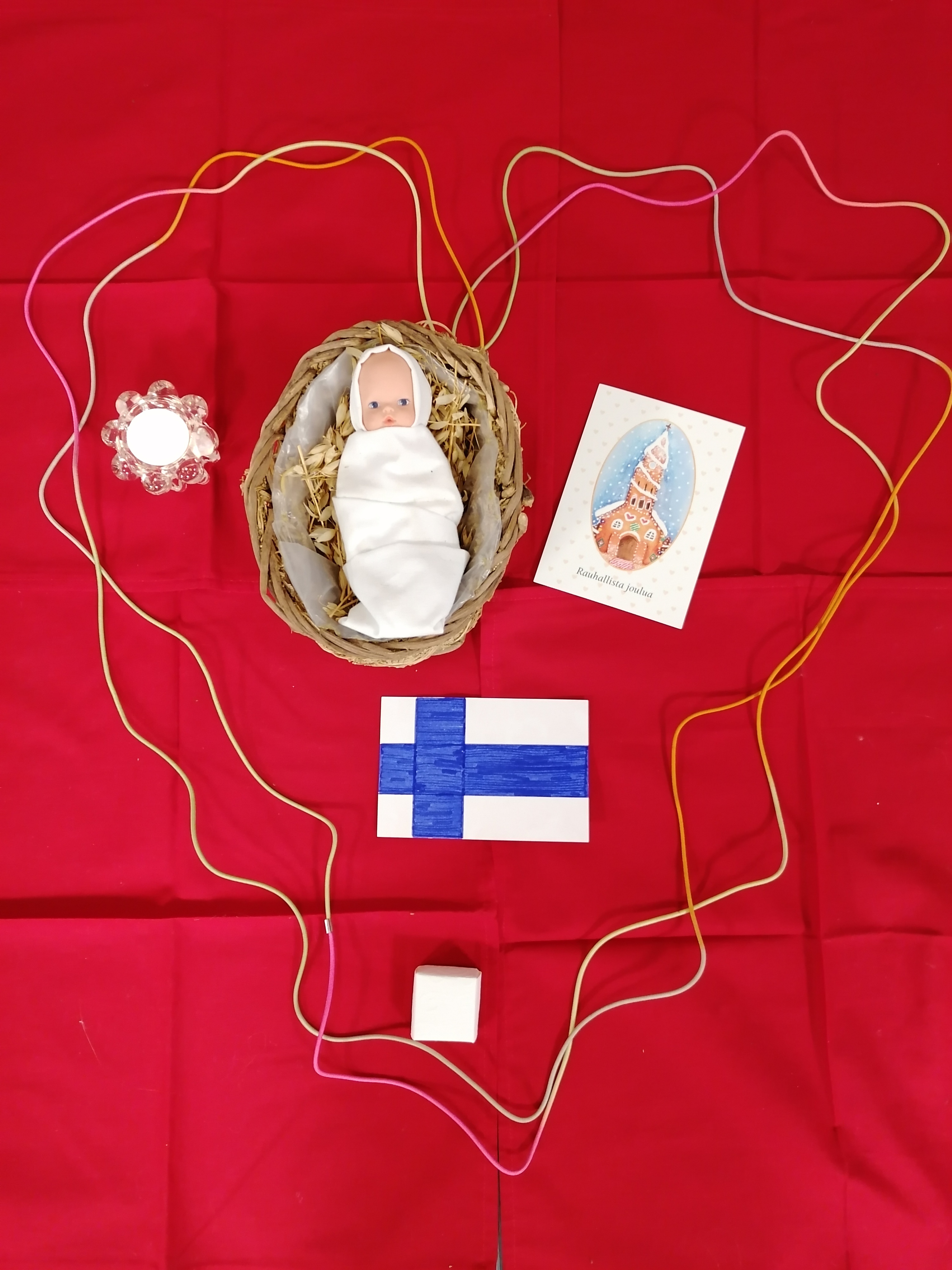 Punaisilla liinoilla sydän nauhasta, jonka sisällä Jeesus-vauva,kynttilä, joulukortti,Suomen lippu,joulukortti