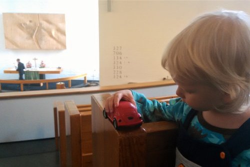 Kolmivuotias poika katselee punaista leikkiautoa Oriveden kirkon lehterillä.