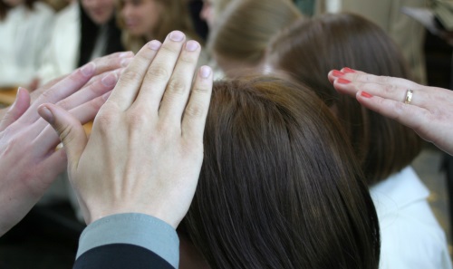 Kummit pitävät käsiään konfirmoitavan nuoren pään päällä. Lähikuva käsistä.